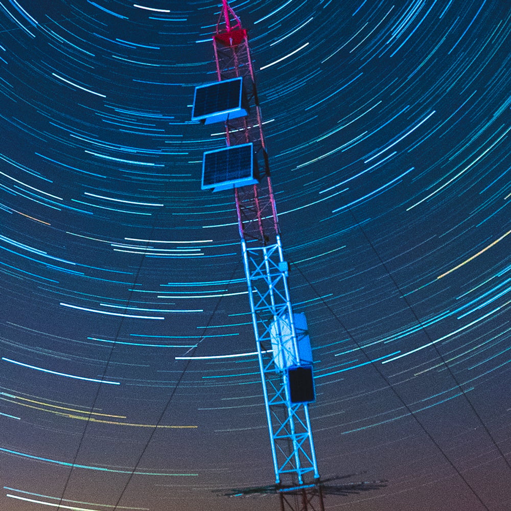 An antenna at dusk with dramatic star trails in the sky above