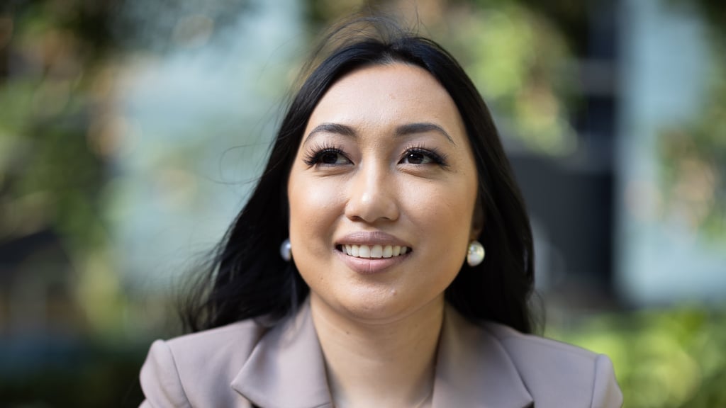 Close-up of Arhita in a light brown suit in front of trees, looking into the distance
