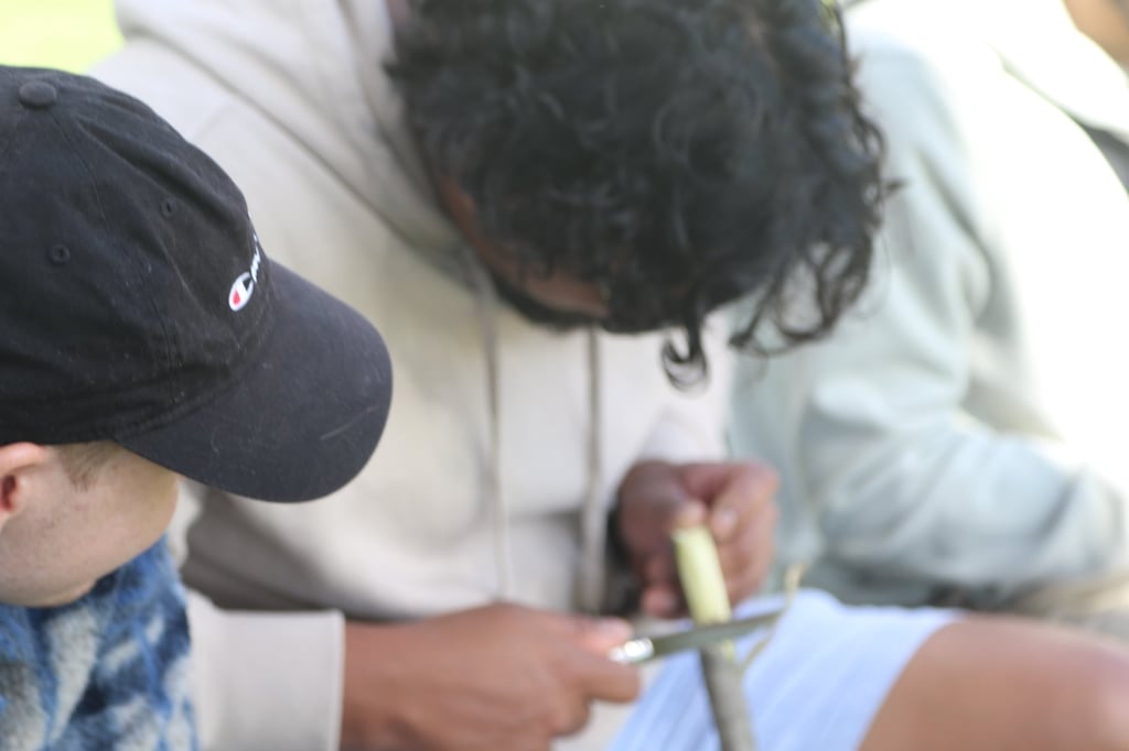Close-up of two people carving a stick.