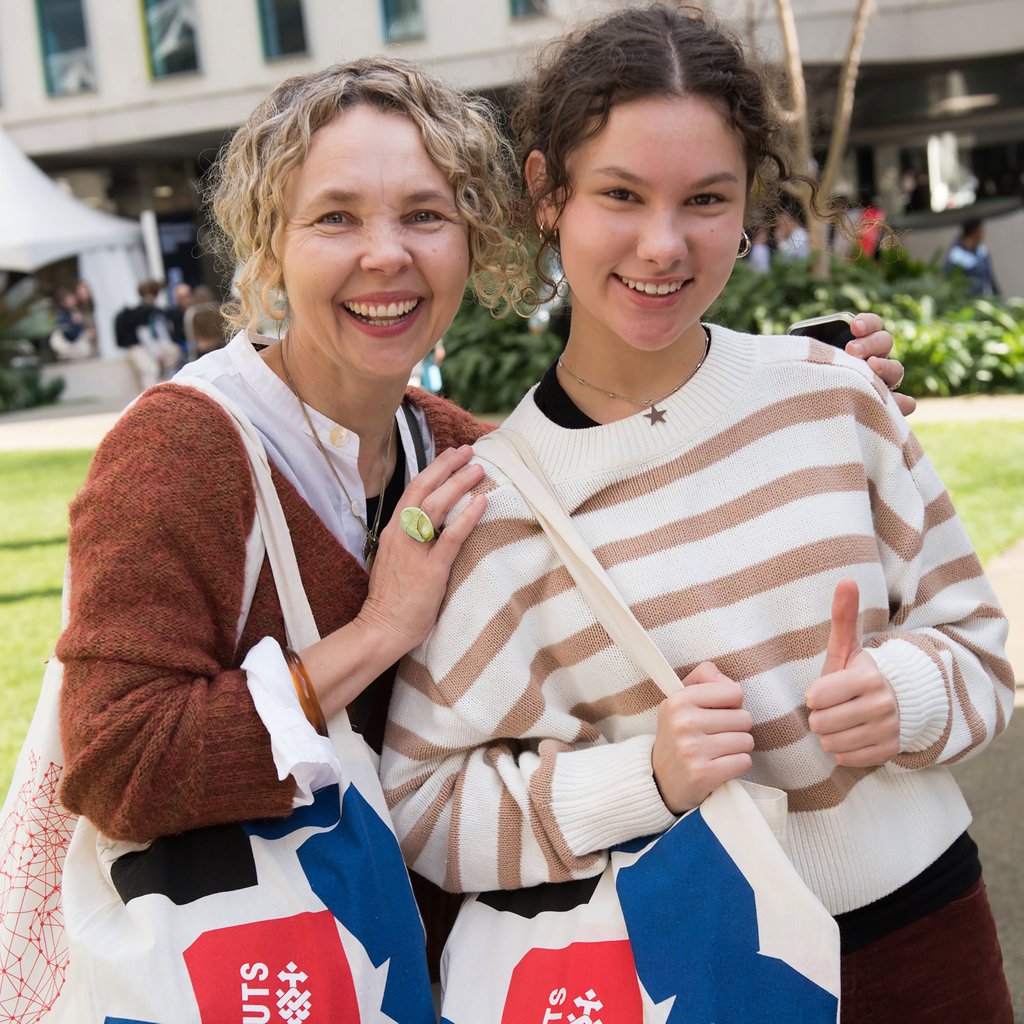 Parent and student at UTS Open Day holding UTS bags standing together and smiling.