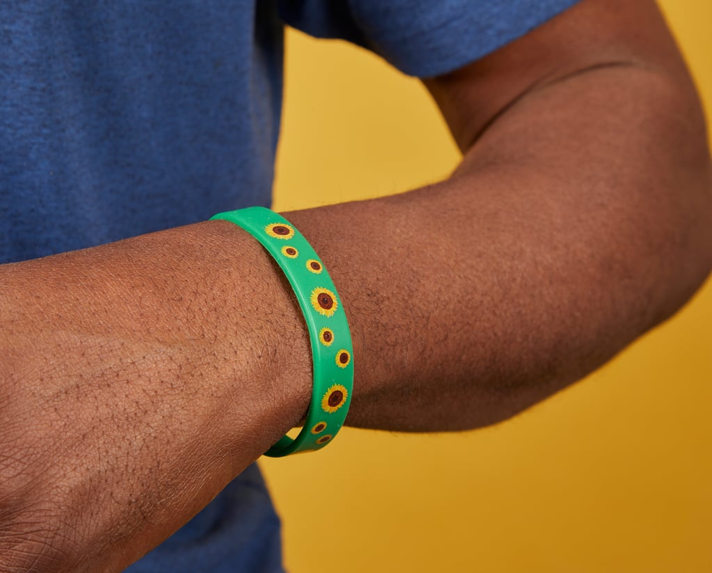 A person wearing a green bracelet with sunflower designs on their wrist, set against a bright yellow background.