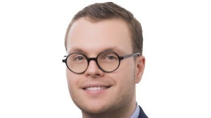 Grant Stollery, UTS Bachelor of Laws student, smiling at the camera, wearing round glasses and a blue shirt and grey suit.