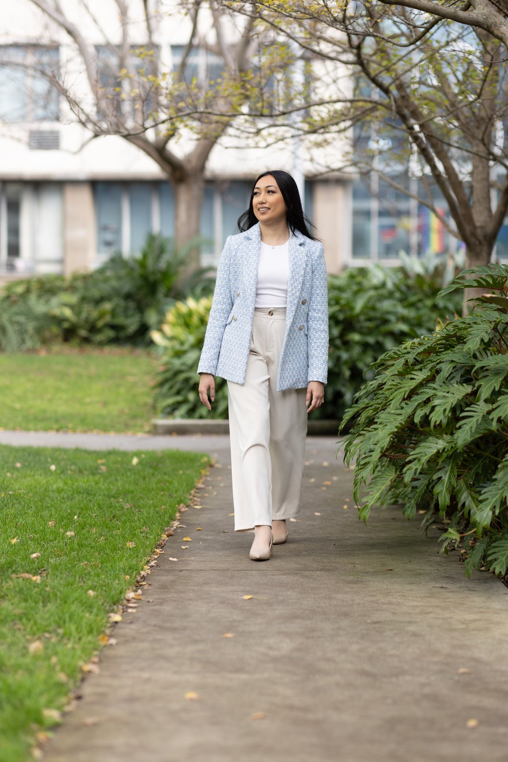 Arhita, wearing a light blue blazer and beige trousers, walks through a garden
