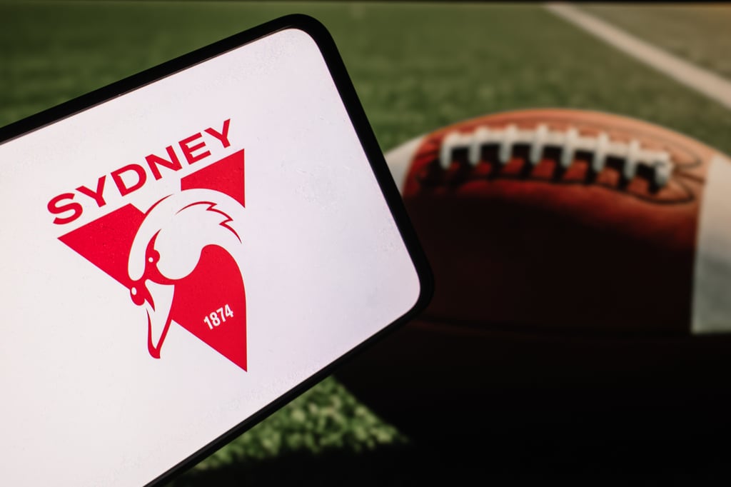 Sydney Swans team logo on phone screen with ball on the field background.
Picture: Ployker/Adobe Stock