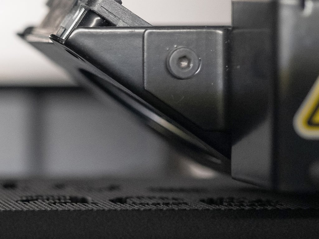 3D print head and black plastic part in focus showing material deposition and printing in process