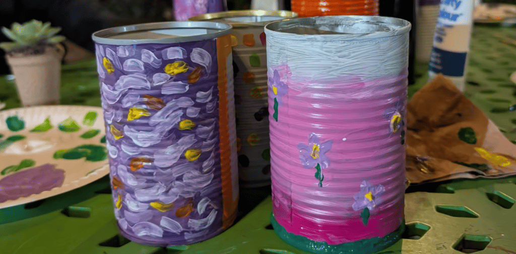 Recycled tin cans painted with colourful floral designs on a craft table.