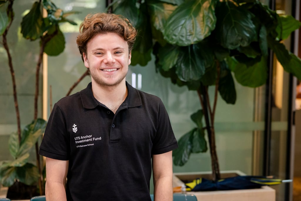A business student stands smiling to camera in their black "UTS Anchor Fund" shirt.