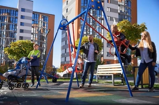 Adults and children enjoy a sunny day at a modern playground in an urban residential area.
