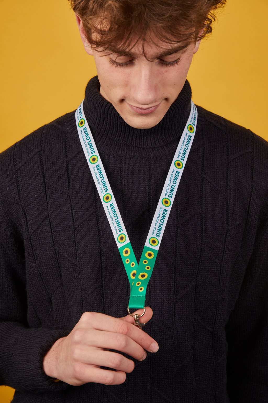 A person looks down while holding a sunflower-patterned lanyard against a textured black sweater.