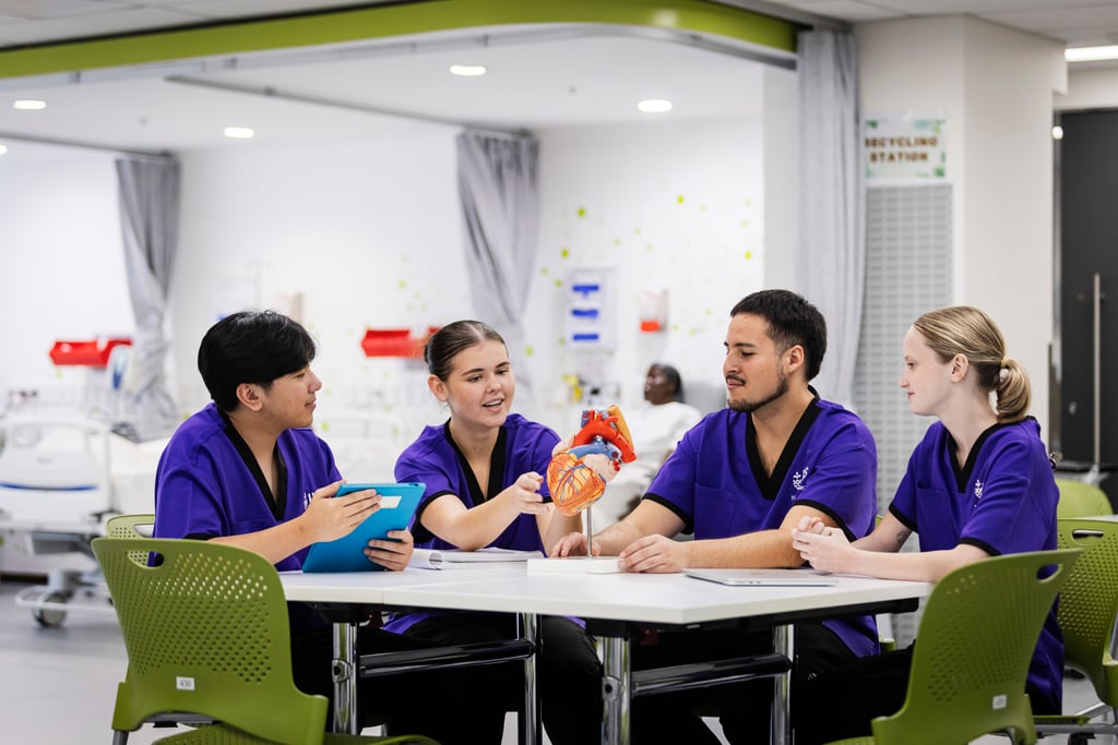 Image of four nursing students. two males and two females sitting around a table in purple scrubs