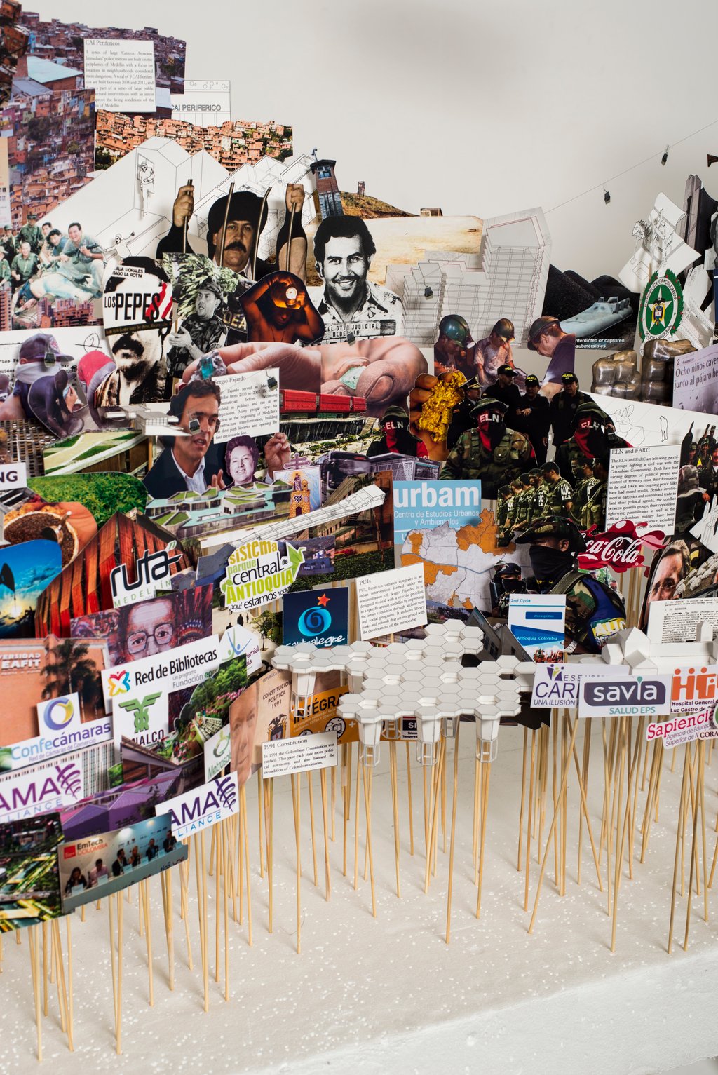 A close up image of the art installation representing the city of Medellin consisting of pictures on paper and folded paper artefacts mounted on sticks of varying heights and embedded in a flat white base.