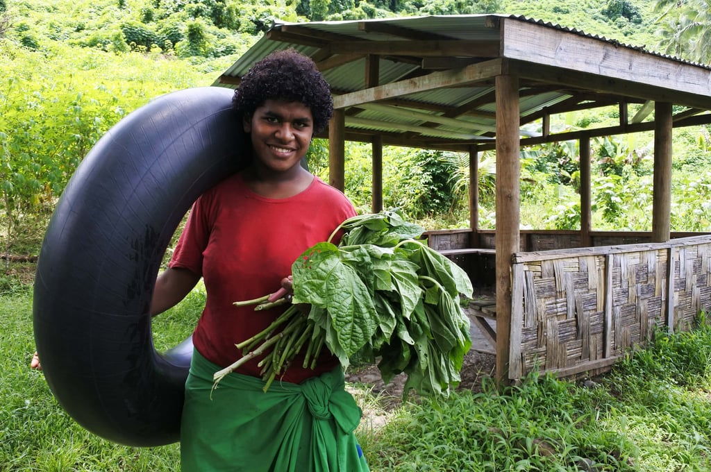 Smiling Fijian woman holding plants and an inflatable tyre.
