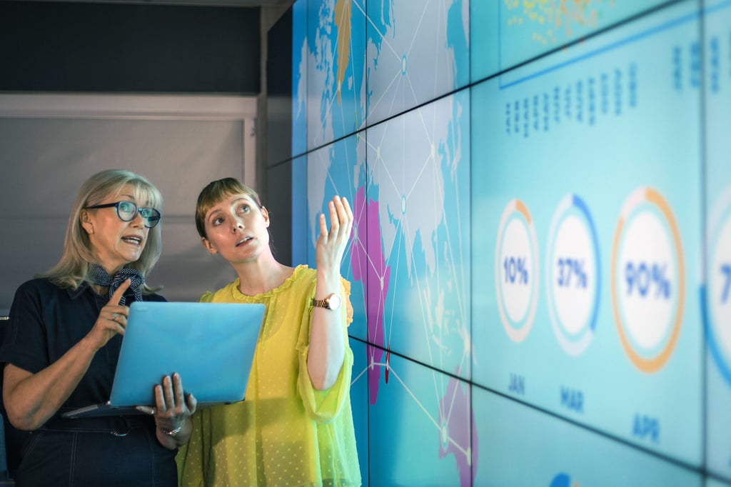 Two professionals collaborate while reviewing data visualisations on a large digital display during a presentation.