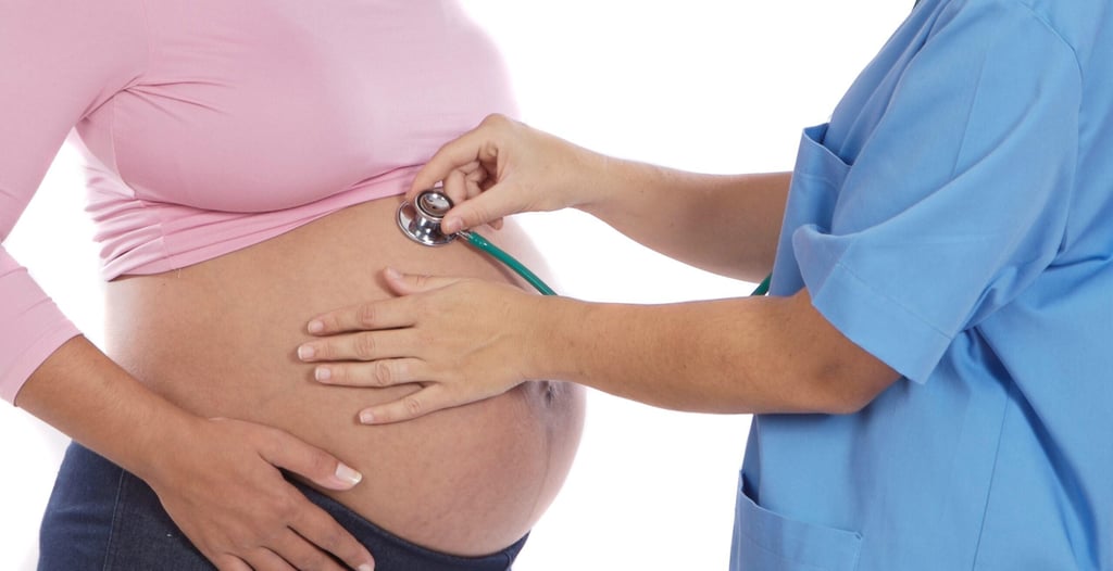 A healthcare professional in blue scrubs uses a stethoscope to listen to a pregnant woman's belly, conveying care and attentiveness in a medical setting.