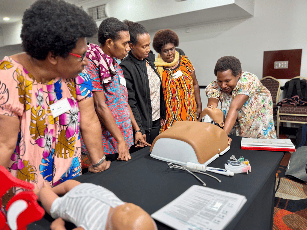 Participants gather around a medical training mannequin on a table.