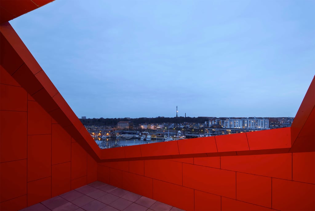 Looking out from the Aarhus Student Housing several floors up through the red painted concrete exterior over the local area in the evening light.