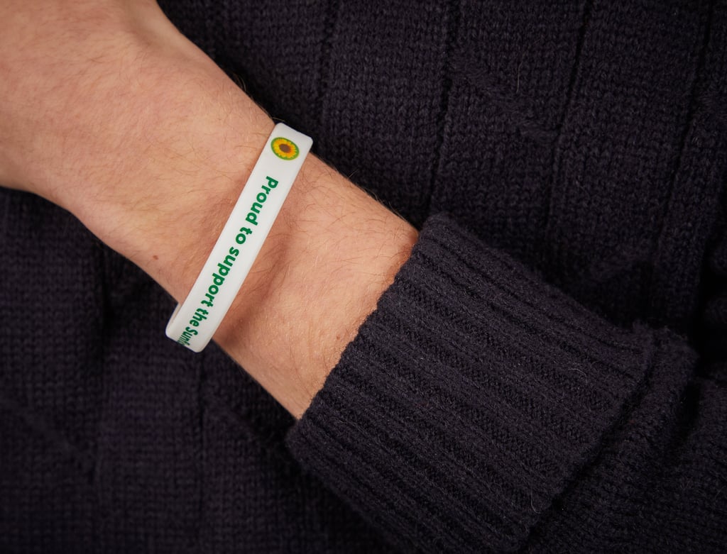 A person wearing a white bracelet with green text that reads "proud to support" alongside a yellow sunflower