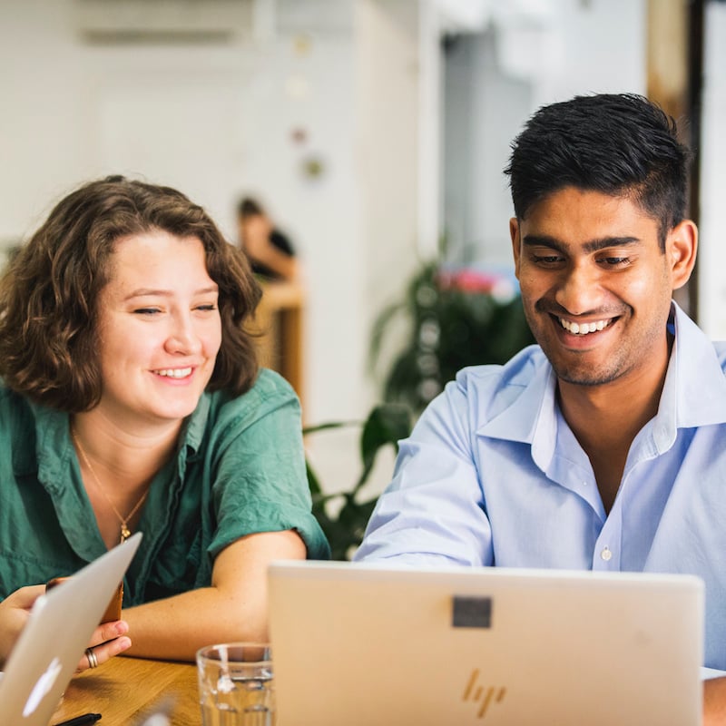 Two people smiling and looking at a shared laptop