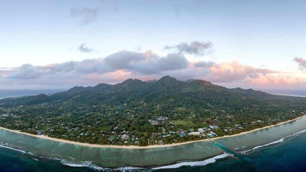 Aerial view of a lush, mountainous island surrounded by a turquoise ocean under a pastel-hued sky at dawn, conveying serenity and natural beauty.