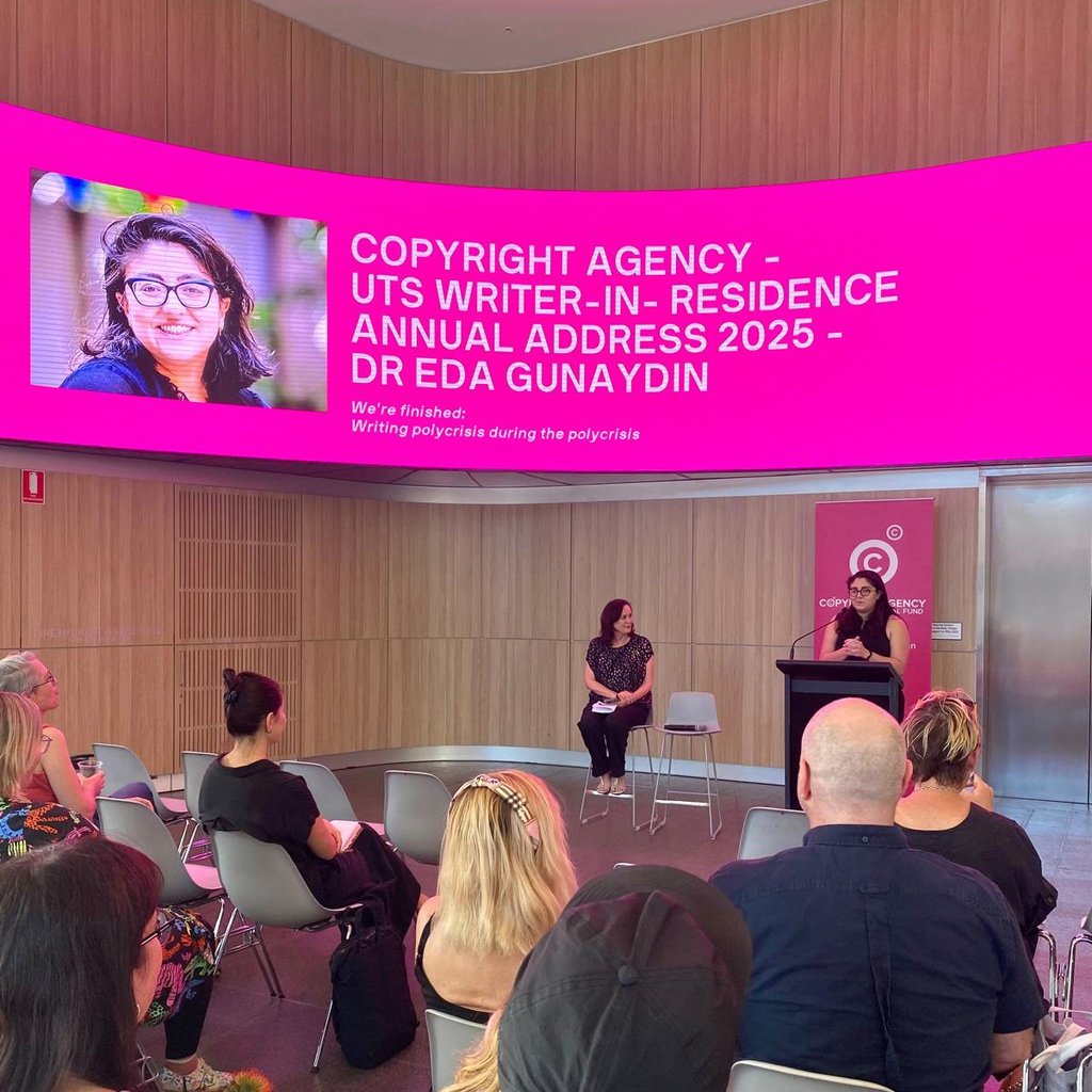 A speaker addresses a seated audience in a modern room, beneath a large screen displaying "Copyright Agency - UTS Writer-in-Residence Annual Address 2025."