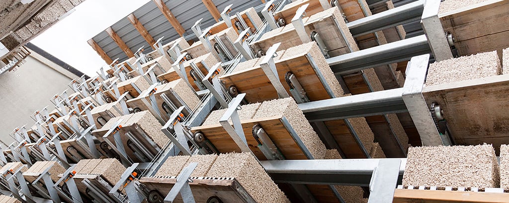 Rows of concrete blocks with embedded steel beams are stacked in a manufacturing facility. The industrial setting conveys precision and efficiency.
