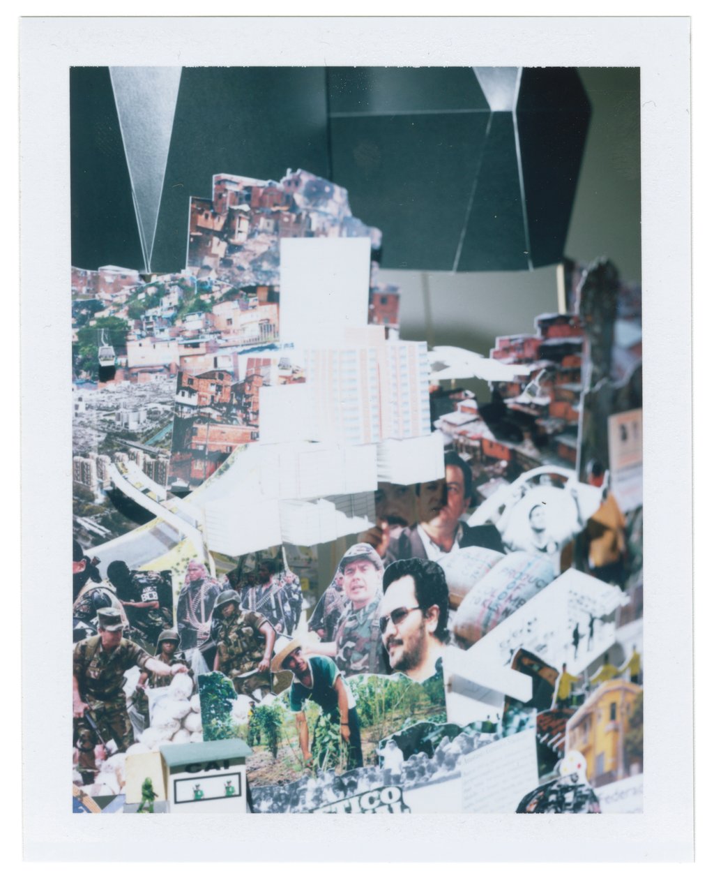 A framed photograph of another section of the art installation representing the city of Medellin consisting of pictures on paper and folded paper artefacts mounted on sticks of varying heights and embedded in a flat white base.