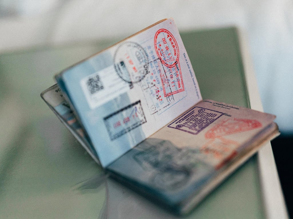 Open passport with several colourful entry and exit stamps on its pages, lying on a reflective glass surface.