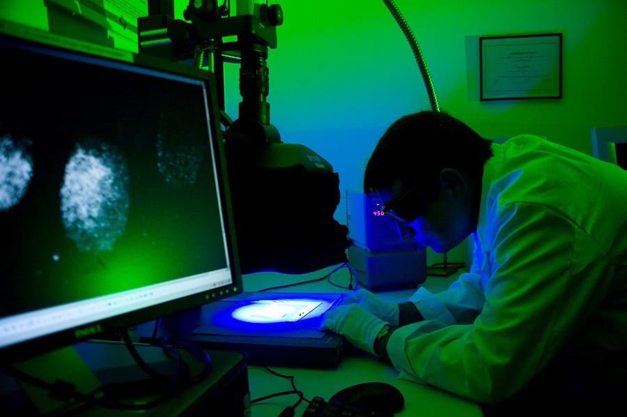 Man in lab coat looking though a microscope in a darkened science lab
