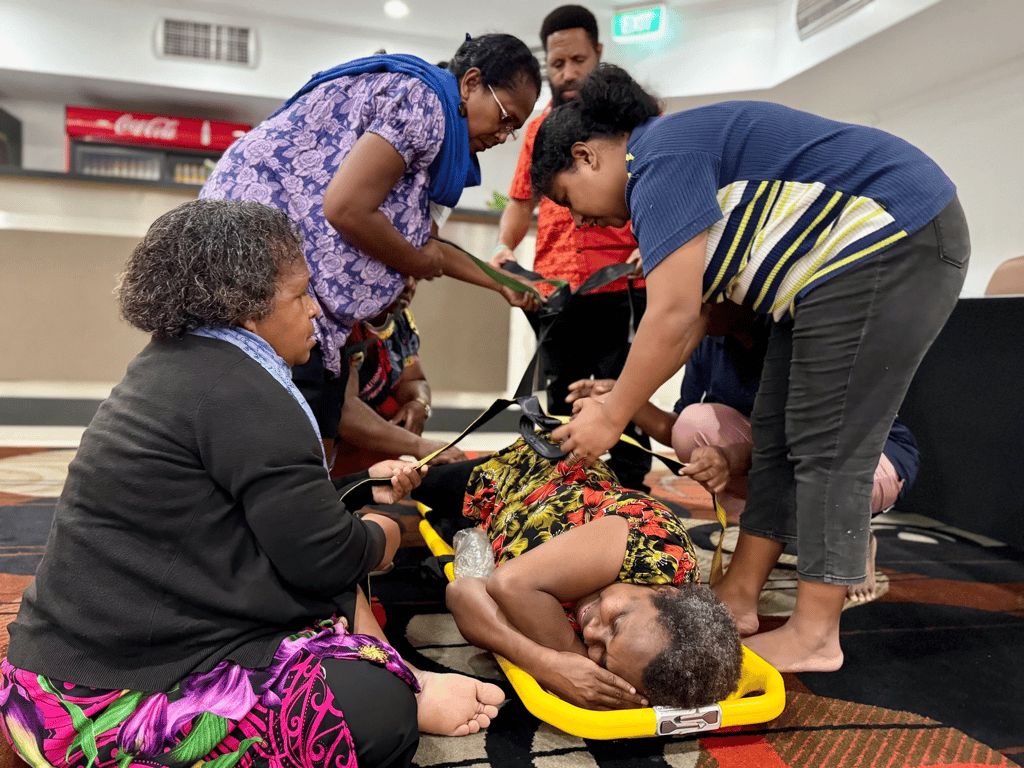 Attendees assist a person on a yellow stretcher during a training exercise.