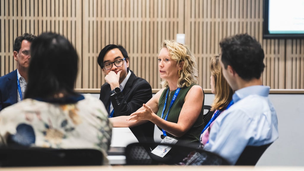Lauren Solomon pictured in discussion with symposium attendees. Lauren is sitting in a table.