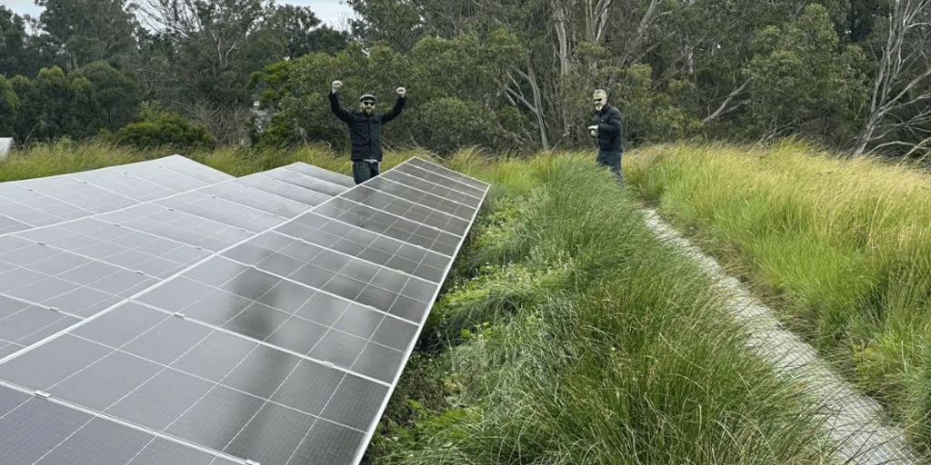 Two people standing beside solar panels surrounded by native grasses and trees.