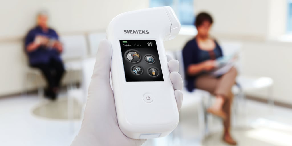 A gloved hand holds a handheld medical device with a touchscreen display; two people sit in the blurred background on white chairs in a waiting area.