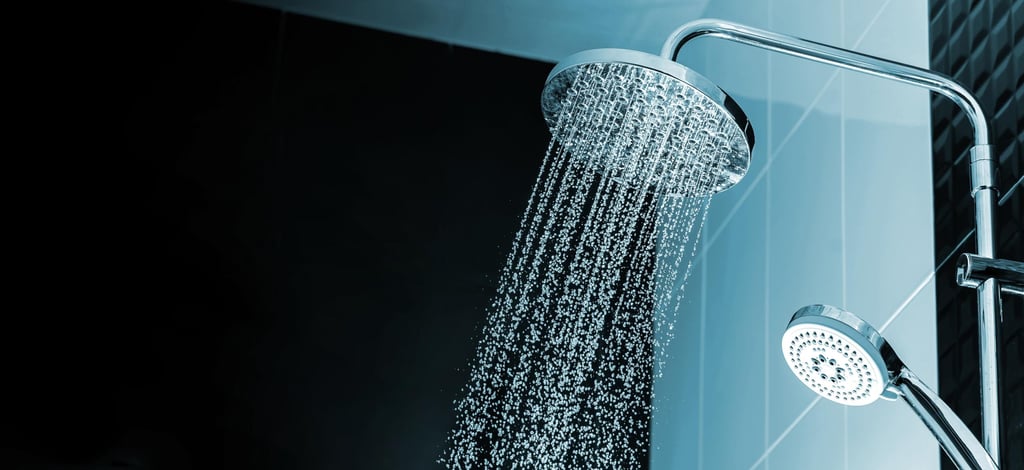 Dual shower heads with cascading water in a modern bathroom, featuring sleek chrome fixtures and dark tiled walls.