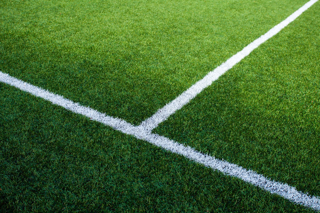Close-up of a sports field showing bright green artificial turf with two white boundary lines intersecting at a corner marking.