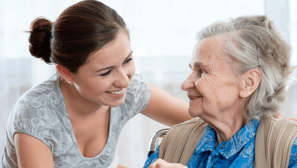 Elderly lady with grey hair is smiling at her carer.