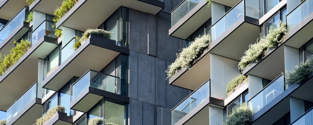 Modern apartment building featuring glass balconies with lush green plants. The geometric design and greenery create a sleek, vibrant aesthetic.