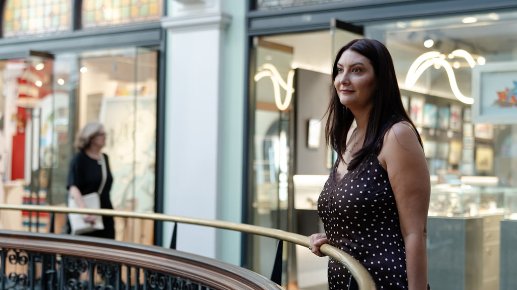 Alison Gibson stands beside a balcony railing inside Sydney's Queen Victoria Building, with retail storefronts and shoppers visible in the background.