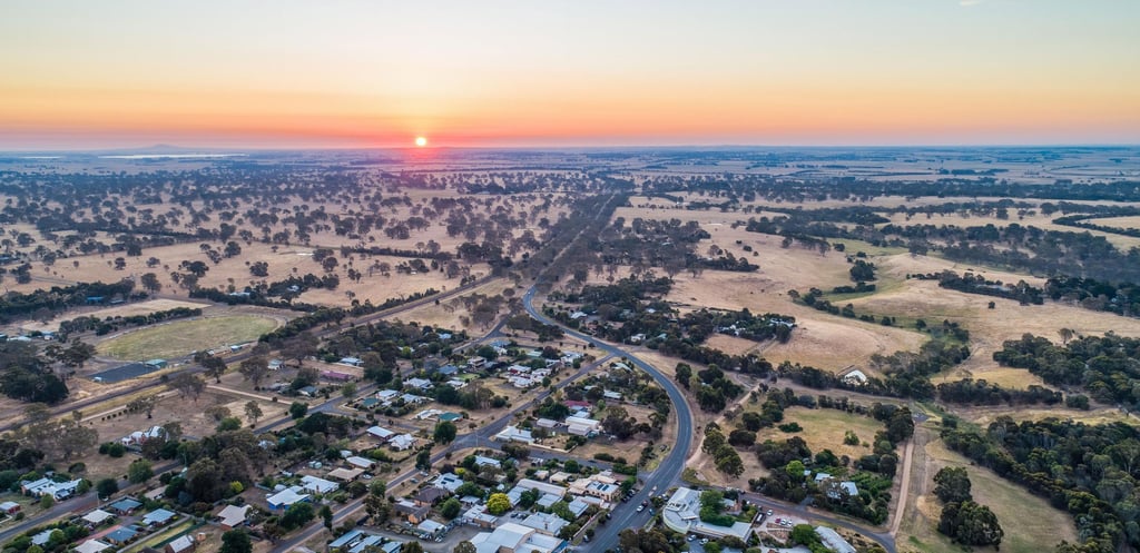 Aerial view of a rural landscape at sunset, with a road winding through fields and a small town. The sky is orange and peaceful, creating a serene atmosphere.