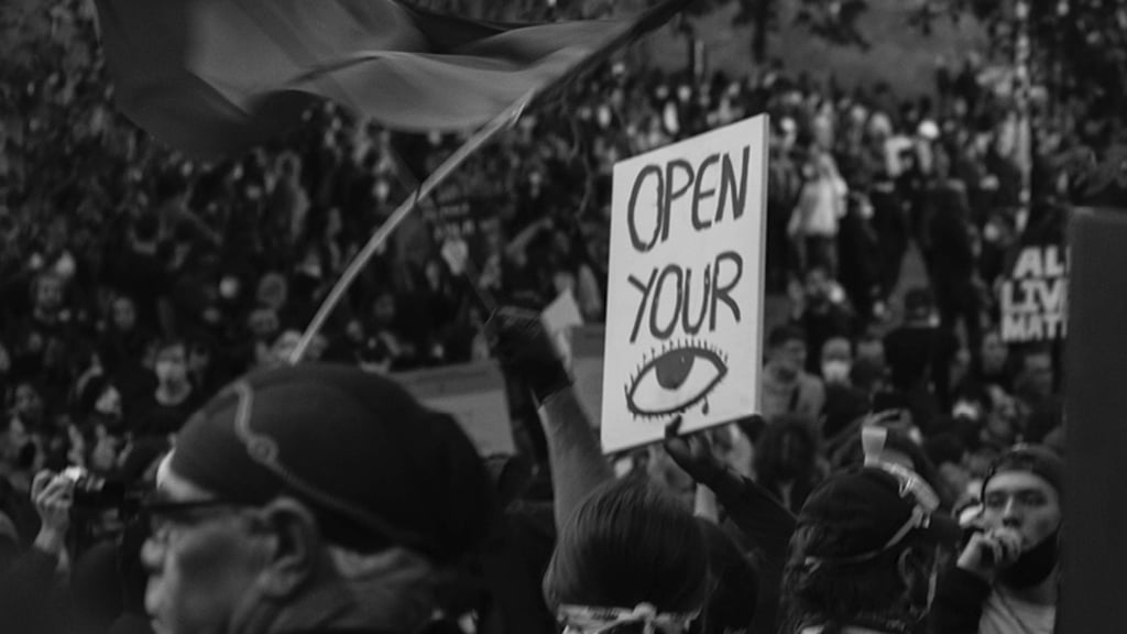 Person holding up a sign which reads "Open your eyes"