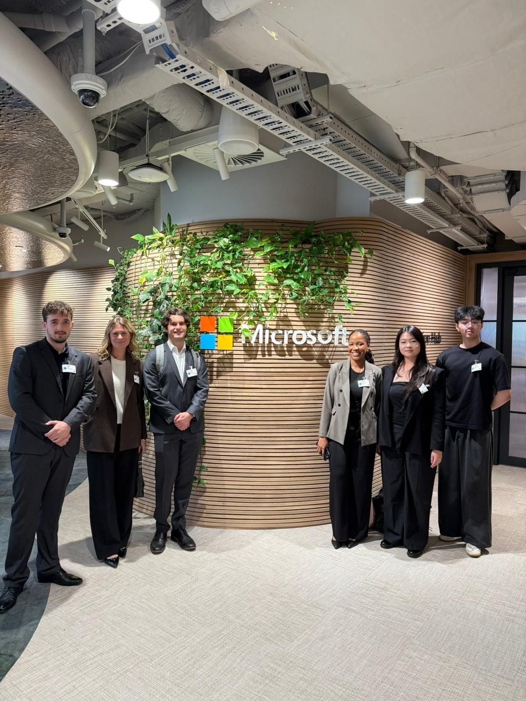 6 students in formal attire pose in front of a Microsoft logo