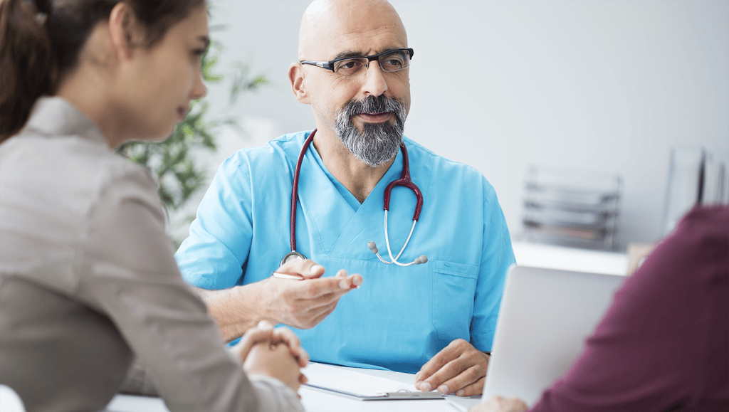 Doctor wearing scrubs talks to patient.