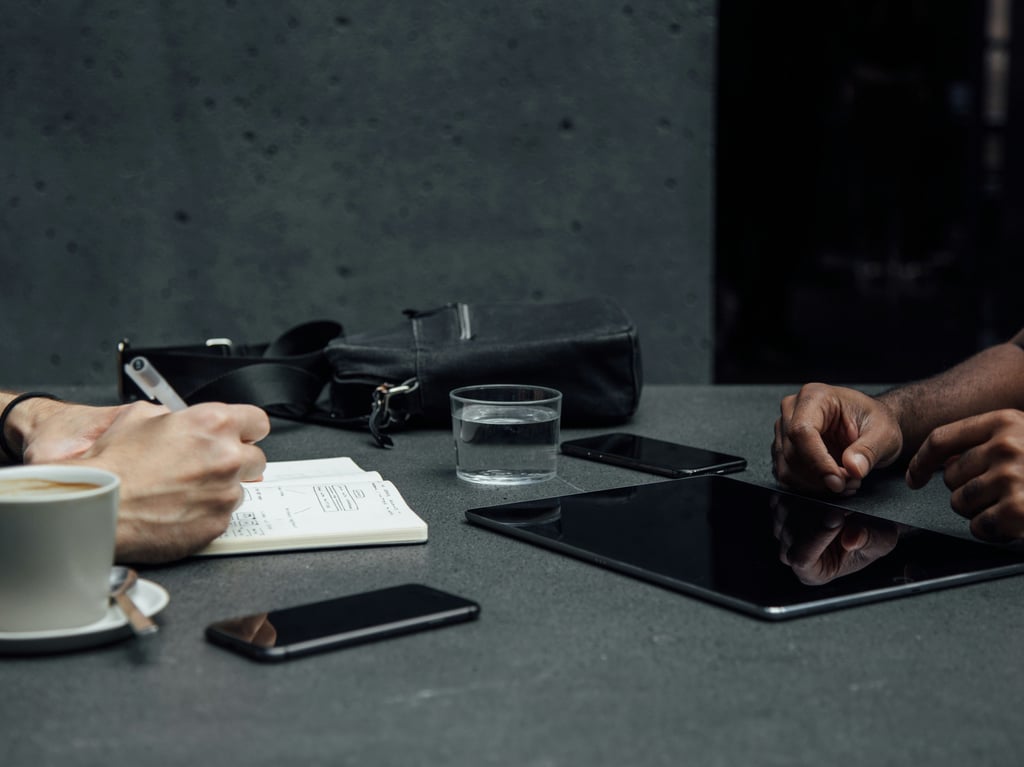 Two people sitting at a desk with electronic devices, one taking notes. Picture: Unsplash