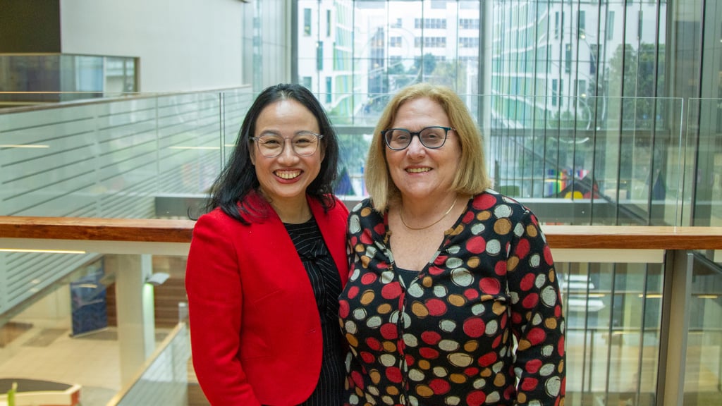 Two women stand on one of the air bridges in Building 10, smiling at the camera with arms around each other