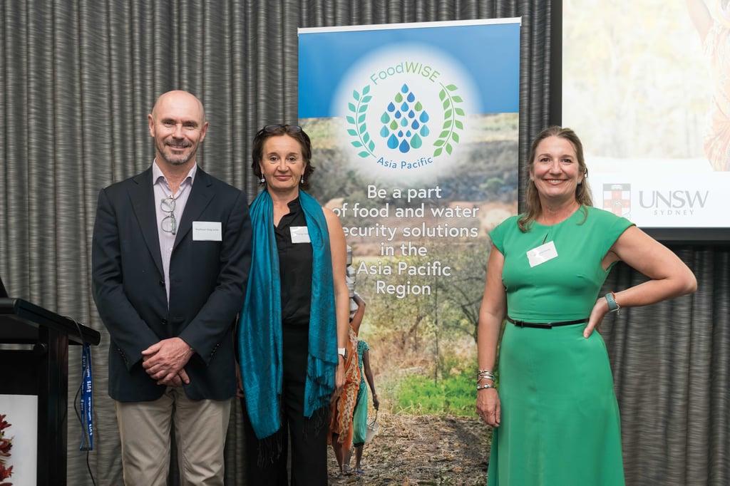 Three people stand smiling in front of a "FoodWISE Asia Pacific" banner promoting food and water security in the Asia Pacific region.