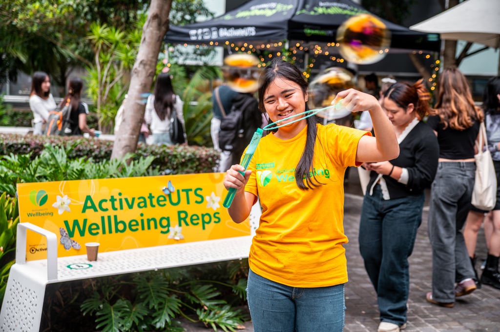 Person creating large soap bubbles at an ActivateUTS Wellbeing Reps stall during an outdoor campus event.