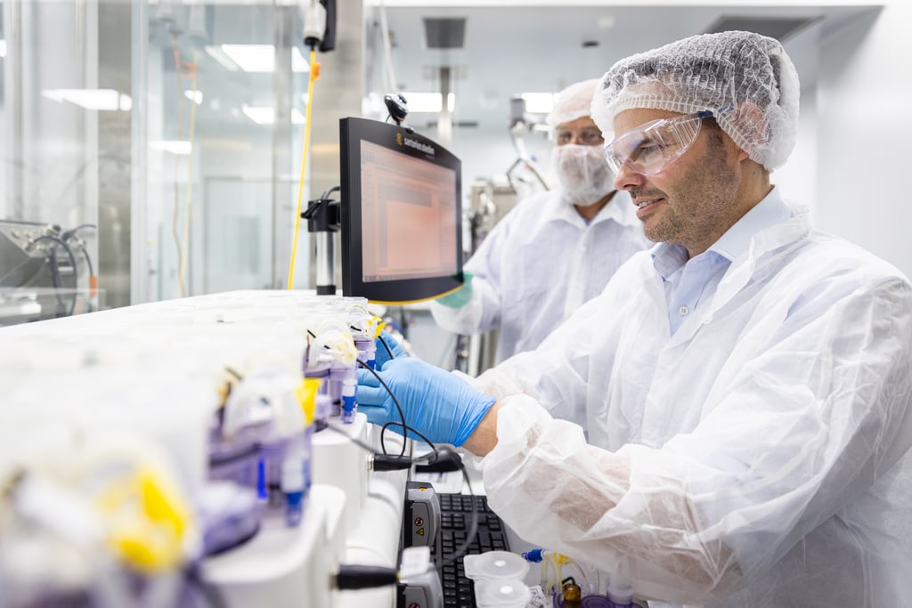 Two researchers wearing protective clothing, hair nets, gloves and safety glasses operate laboratory equipment in a cleanroom.