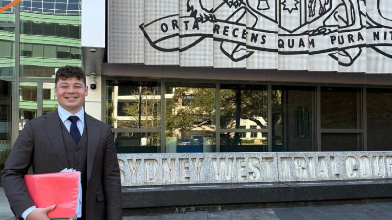Deon, wearing a three-piece brown suit and blue tie, stands proudly outside the Sydney West Trial Court.