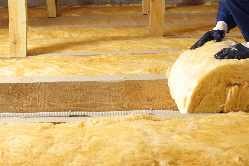 A person wearing gloves installs yellow fiberglass insulation between wooden beams in an attic, creating a clean and efficient energy-saving setup.