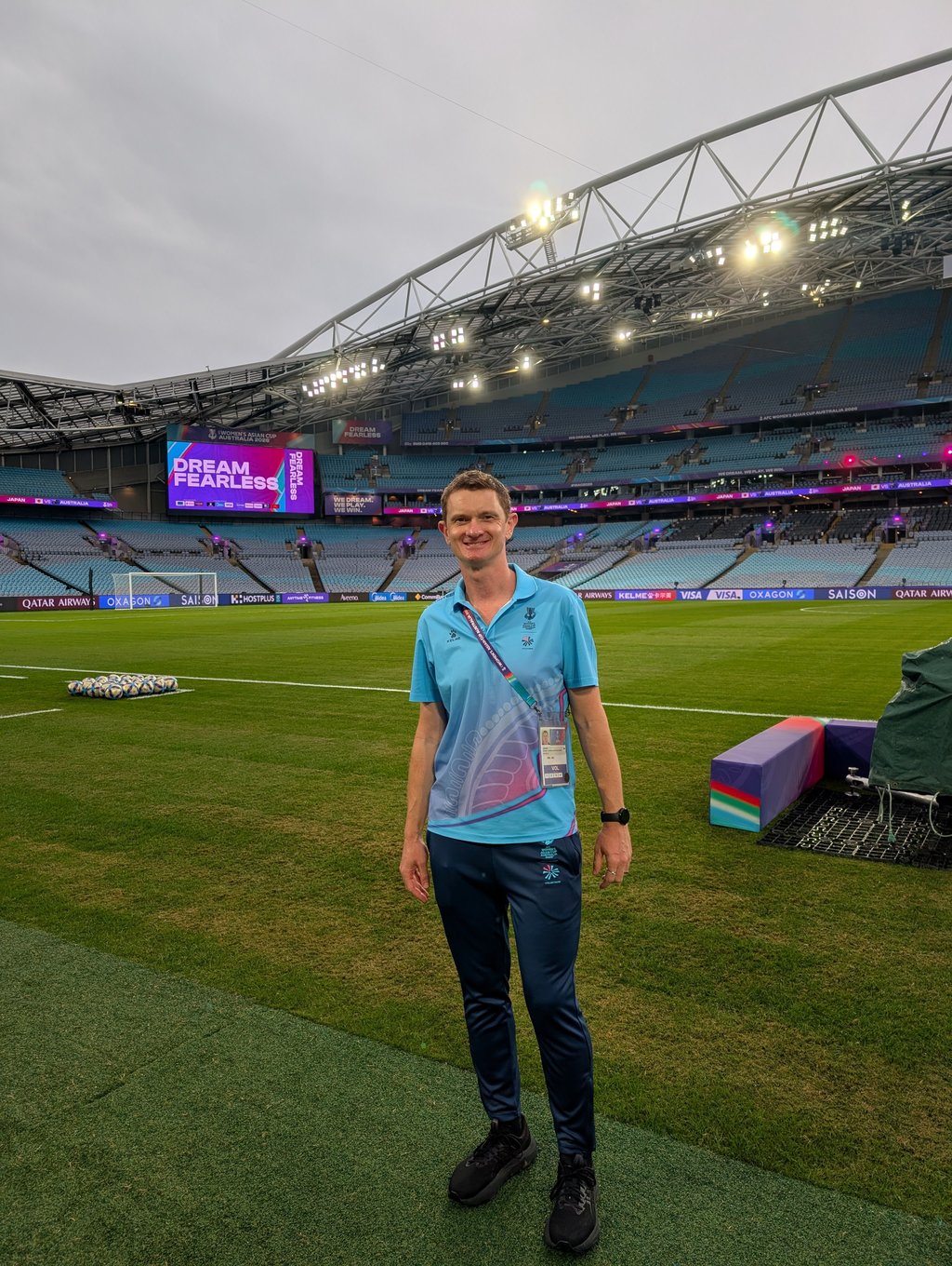 Leif Smith is standing on the sideline of the Stadium Australia before a soccer match starts. A screen in the background reads "Dream fearless" which is the motto of the Asian Cup tournament.