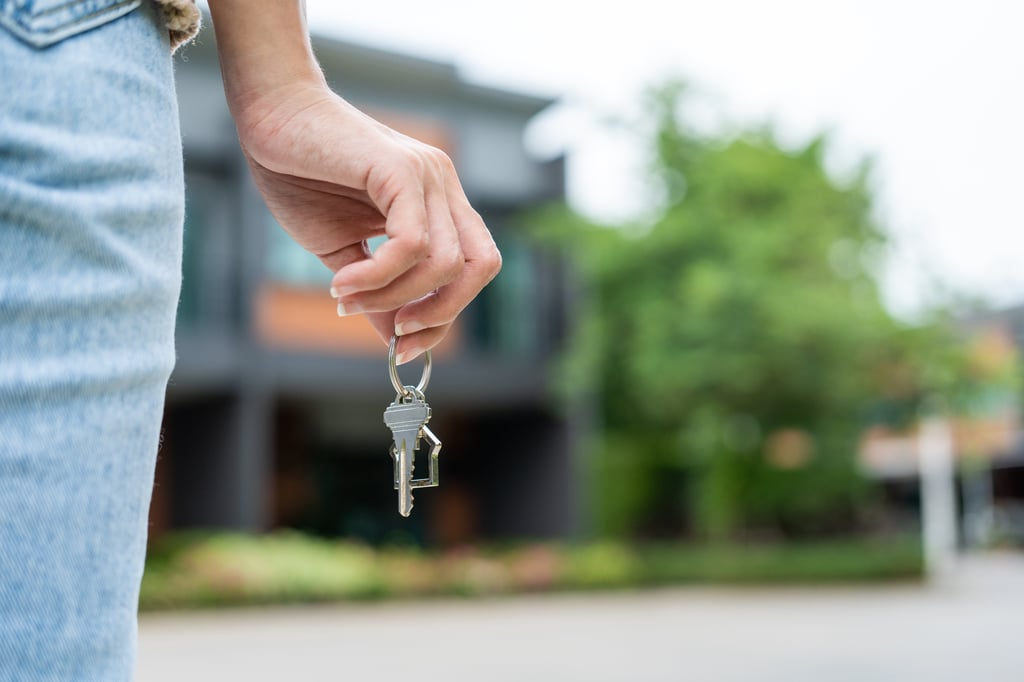 Woman buying or renting new home, holding key front of new house. Picture by Chanakon/Adobe Stock